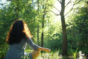 Eine Frau in einem hellblauen Kleid übt sich in der Natur in Achtsamkeit