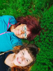 Zwei lächelnde Frauen liegen im grünen Moos