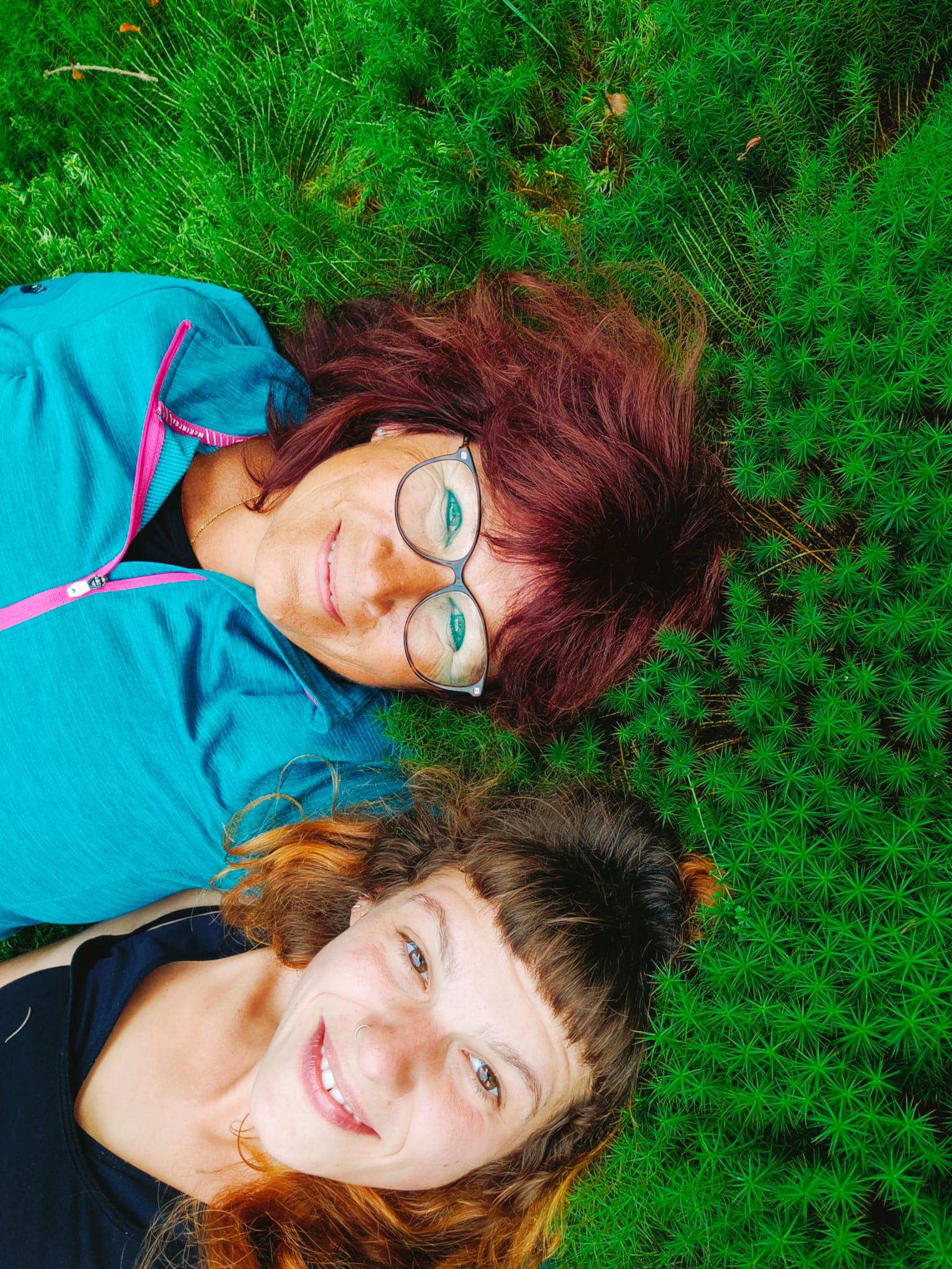 Zwei lächelnde Frauen liegen im grünen Moos