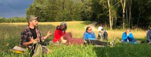 Eine Gruppe von menschen sitzt auf einer Waldlichtung. Ein Lehrer erklärt ihnen etwas