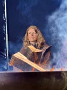 Eine Frau sitzt am Feuer und Rauch zieht vorbei