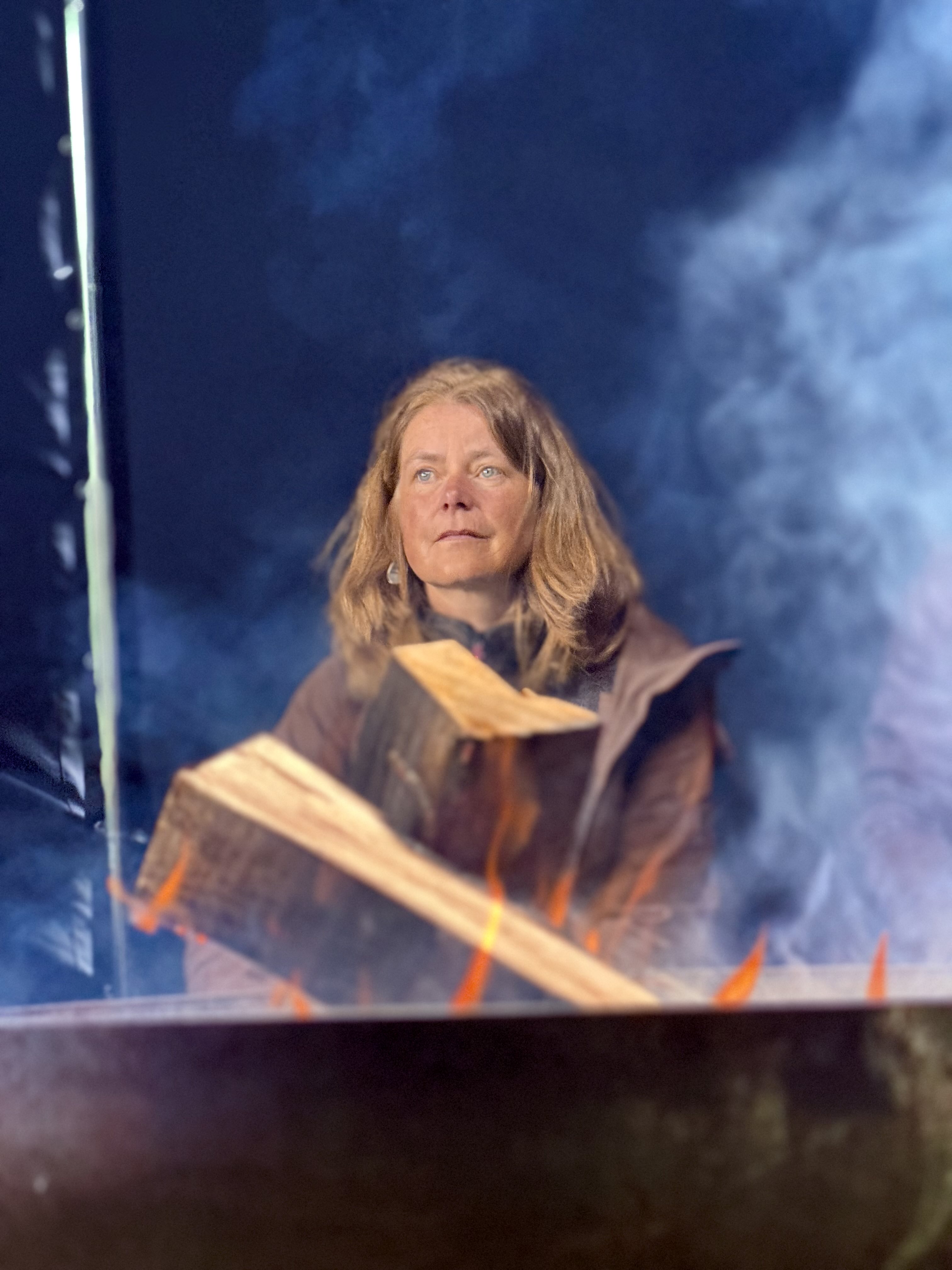 IMG_2170 Eine Frau sitzt am Feuer und Rauch zieht vorbei