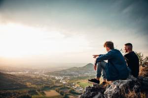 Zwei Naturcoaches sitzen auf einem Felsen und blicken in eine weite Landschaft